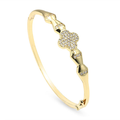 A gold bangle bracelet featuring a central four-leaf clover motif paved with small clear stones, accented with small diamond-like stones along the band, shown on a white background.