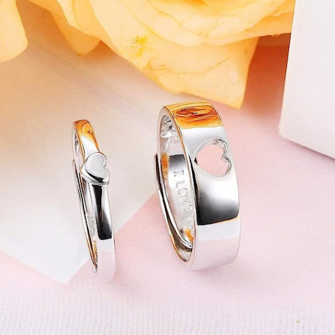 Two silver rings with heart designs on a soft pink background