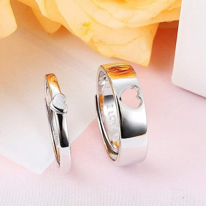 Two silver rings with heart designs on a soft pink background