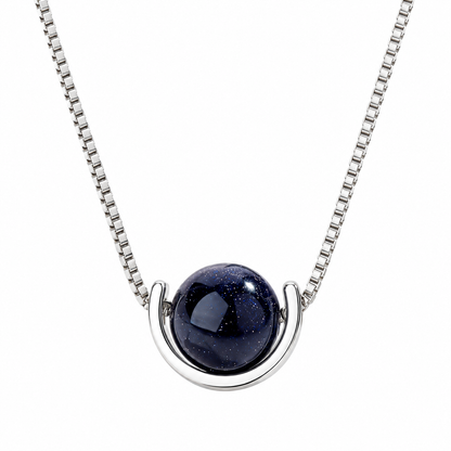 A silver box chain necklace with a modern crescent-shaped silver setting holding a dark blue, starry glass cabochon pendant, shown against a plain white background.