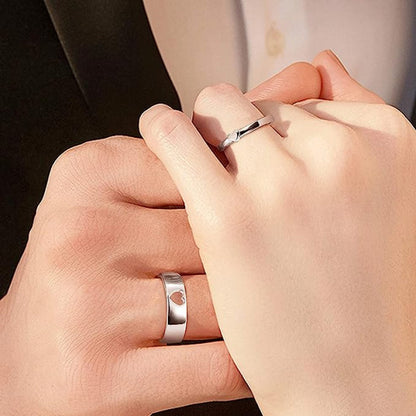 Two hands wearing silver rings with heart designs on a neutral background